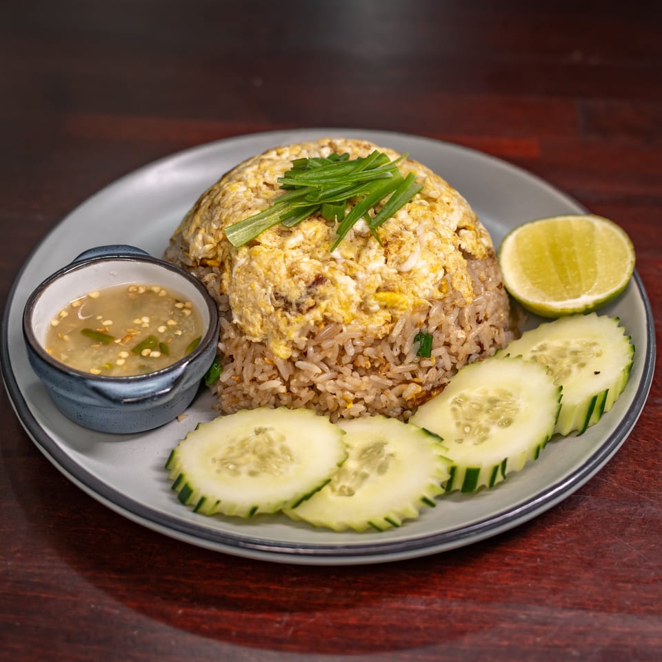 Thai fried rice with scrambled egg, green onions, cucumber slices, lime, and dipping sauce.